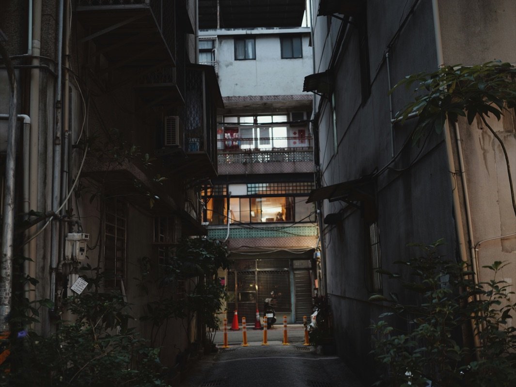 黃昏時分的台灣老巷，巷底公寓亮著一盞溫暖的燈